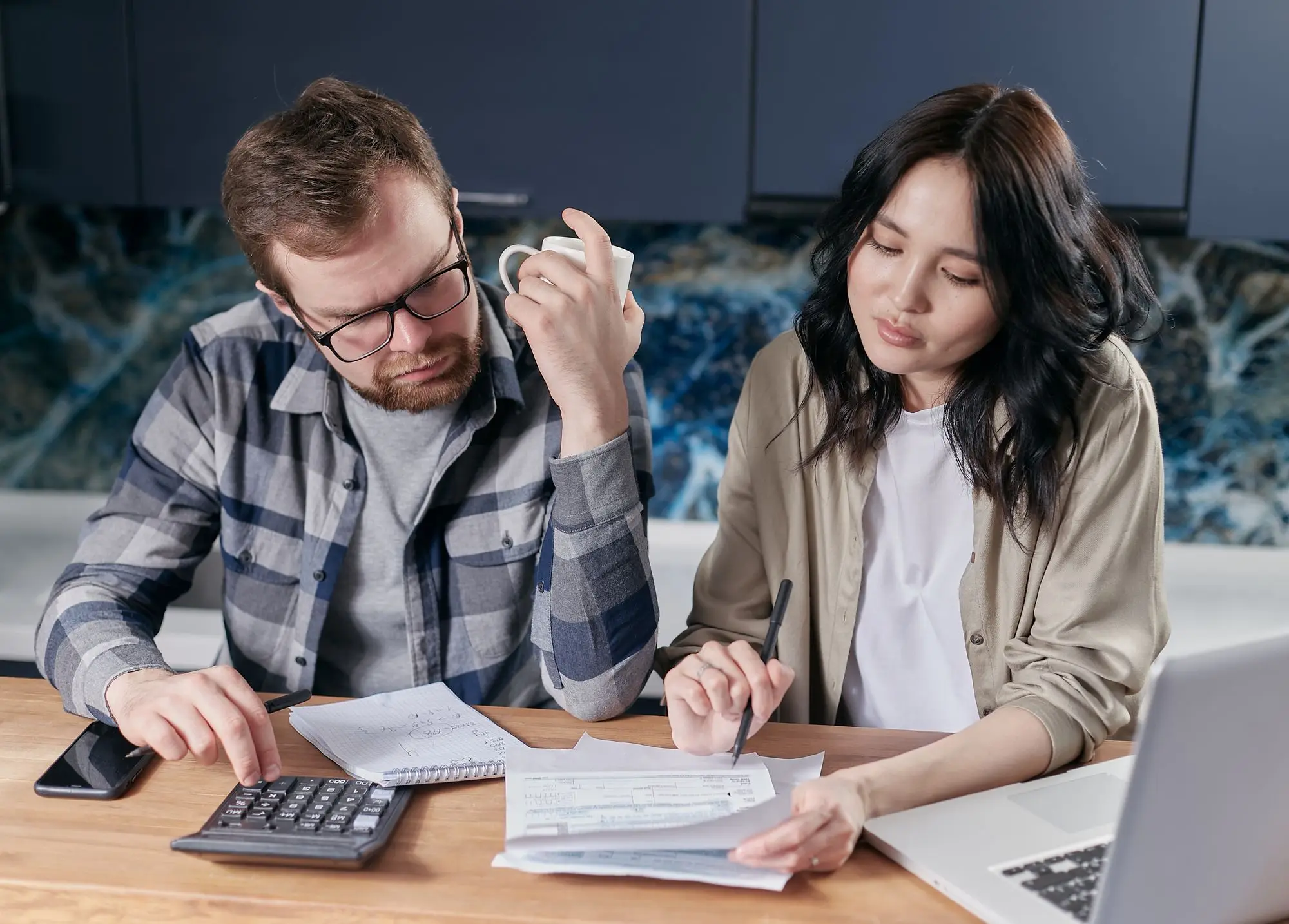 Business owner and partner at the kitchen table with a calculator, laptop and paperwork, working through a personal insolvency agreement before applying for finance