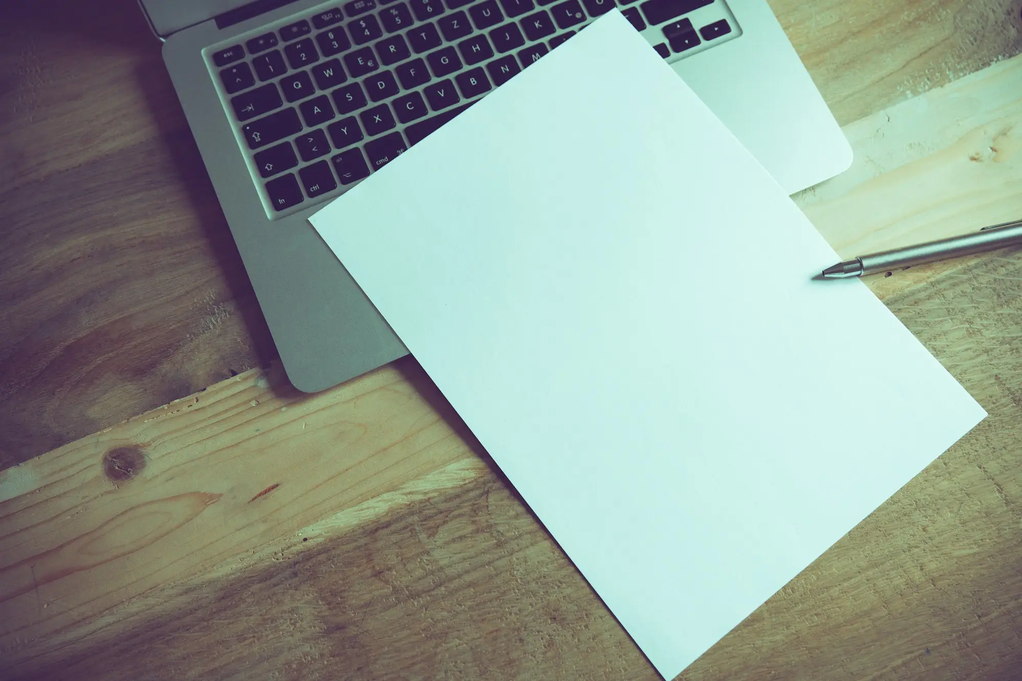 Blank sheet of paper and pen resting on a laptop keyboard, ready for a written letter to a supplier about a payment default