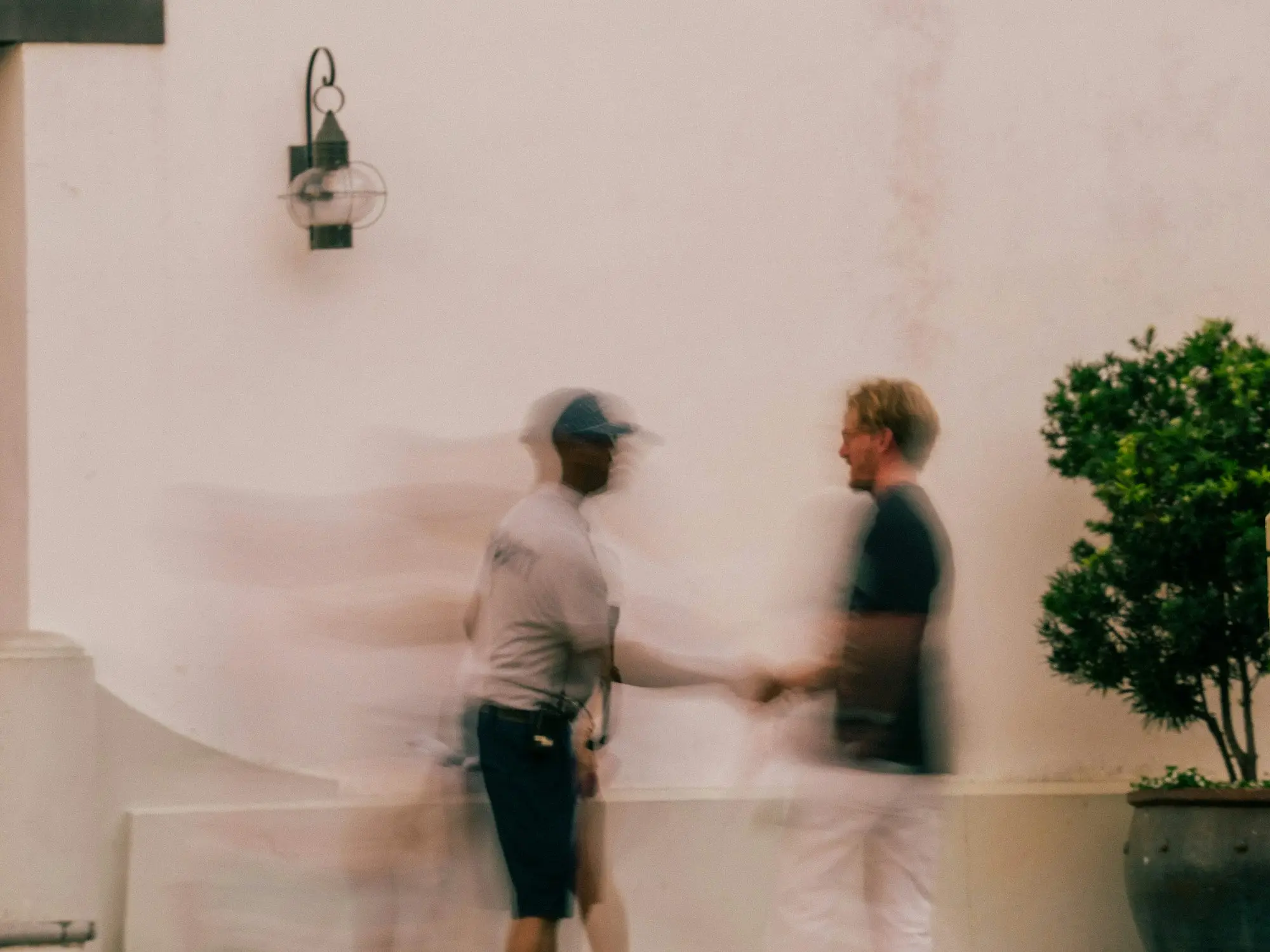 Two people shake hands outside a rendered wall, motion-blurred, sealing a payment agreement